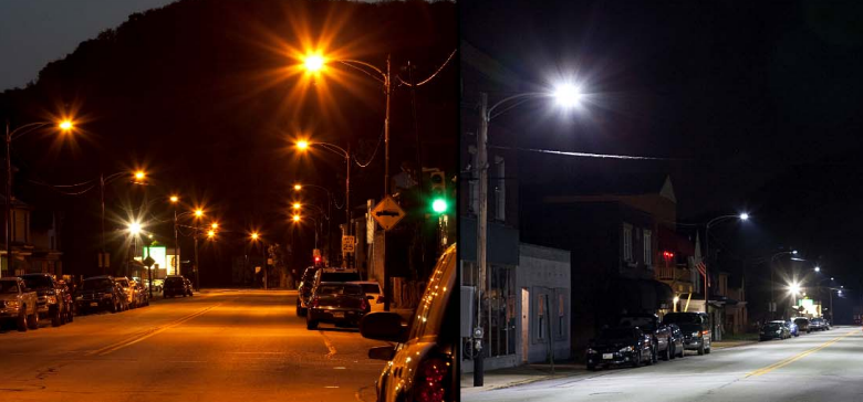A side-by-side comparison photo of a city street lit by old sodium-vapor lamps (orange glow) versus modern white LED lighting